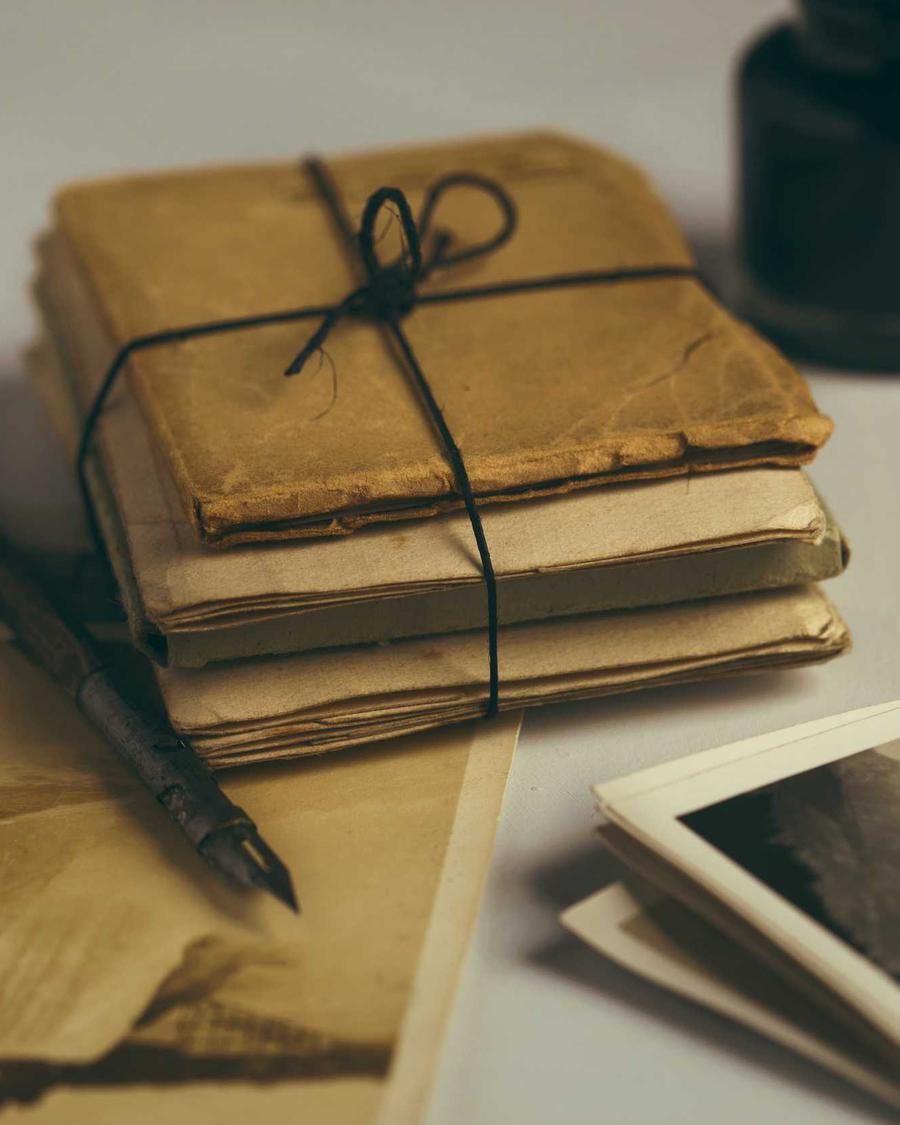 A bundle of letters tied with thread, beside an ink pen and old photographs